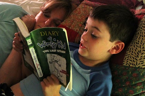 two children reading a diary of a wimpy kid book together while lying down on a couch